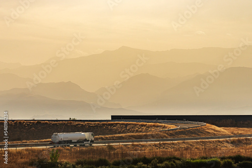 Fuel tanker truck driving along a freeway access with a background of mountains in sunrise mists.