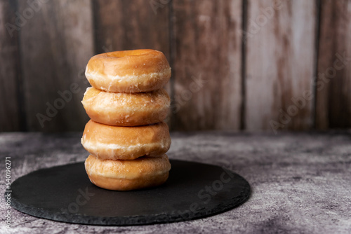 Glazed donuts, placed one on top of the other on a stone plate, with a rustic wooden background.