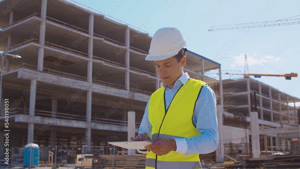 Professional builder standing in front of construction site. Foreman in hardhat helmet and vest. Office building and crane background. Business, real estate and investment. Professional builder standing in front of construction site. Foreman in hardhat helmet and vest. Office building and crane background. Business, real estate and investment.