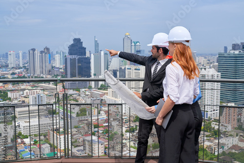 Team of Engineers wear formal suit and safety helmet look to cityscape view building for plan construction
