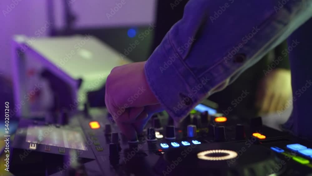DJ turns buttons on mixing console illuminated by neon lights in the nightclub DJ turns buttons on mixing console illuminated by neon lights in the nightclub