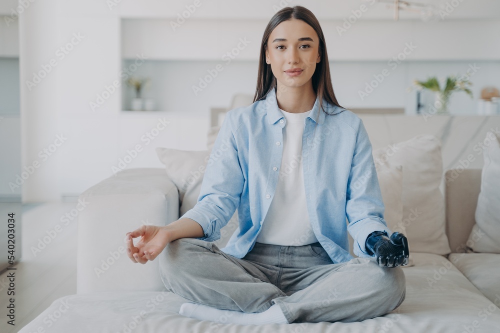 Disabled girl with bionic prosthetic arm does yoga, sitting in lotus pose. Disability, stress relief Disabled girl with bionic prosthetic arm does yoga, sitting in lotus pose. Disability, stress relief