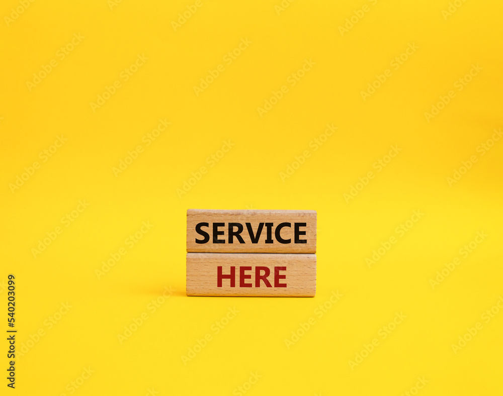 Service here symbol. Concept words Service here on wooden blocks. Beautiful yellow background. Business and Service here concept. Copy space. Service here symbol. Concept words Service here on wooden blocks. Beautiful yellow background. Business and Service here concept. Copy space.