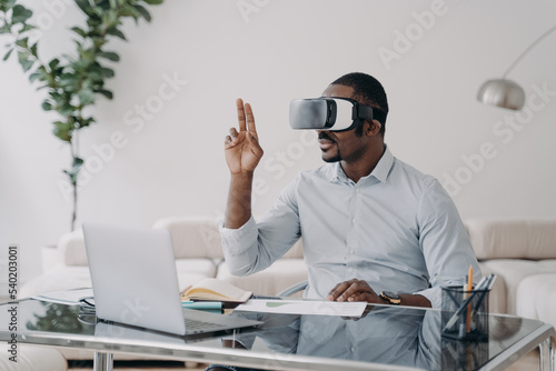 African american man architect in virtual reality glasses works on project in VR on laptop in office