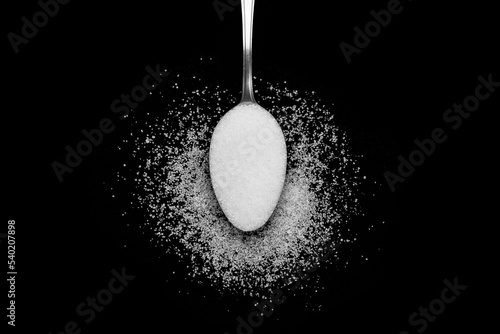 Biały cukier na łyżeczce rozsypany na czarnym tle 