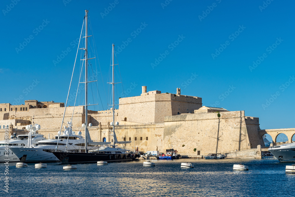 A yacht and sailing boat moored in Dockyard Creek in front of Fort St. Angelo at Birgu (Vittoriosa), Malta.