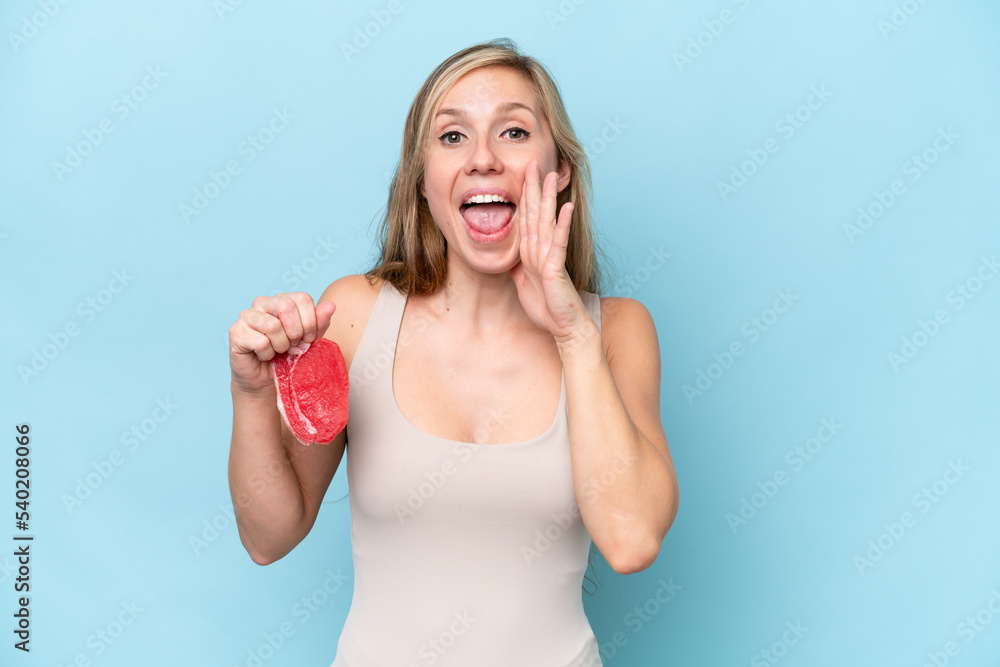 Young blonde woman holding a piece of meat isolated on blue background shouting with mouth wide open Young blonde woman holding a piece of meat isolated on blue background shouting with mouth wide open