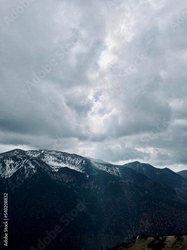 prześwitujące przez chmury światło słoneczne nad ośnieżonymi szczytami gór
