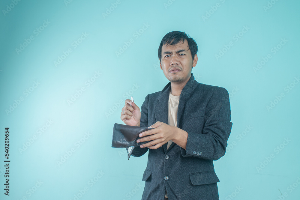 Asian businessman wearing a black suit looks sad because of the contents of his empty wallet. Standing on a blue background Asian businessman wearing a black suit looks sad because of the contents of his empty wallet. Standing on a blue background