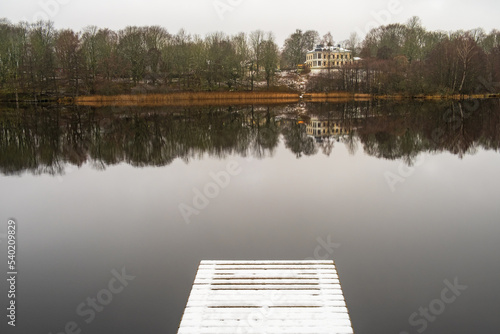 Snowy jetty at a lake with a house on a hill in december light photo