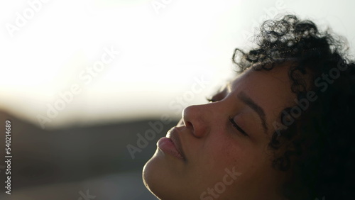 Meditative African American closing eyes in contemplation. A carefree black girl opening eye to sky closeup face