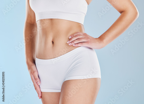 Body, diet and weightloss with a woman in studio on a blue background with her hand on her hip for wellness. Fitness, health and stomach with a model female in underwear for a healthy lifestyle