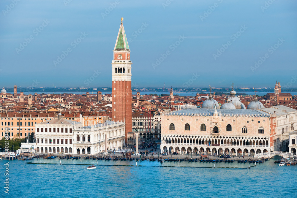 Fototapeta premium Aerial view of Doge's Palace or Palazzo Ducale and Campanile di San Marco, St. Mark's Campanile or bell tower and water of Venetian lagoon with gondolas. Bright day with blue sky and sea.