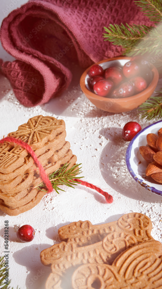 Speculoos or Spekulatius, Christmas biscuits, with cranberry berries, almonds on a table with kitchen towel, fir twigs. Traditional German sweets, cookies for Christmas or Advent, wintertime snacks.