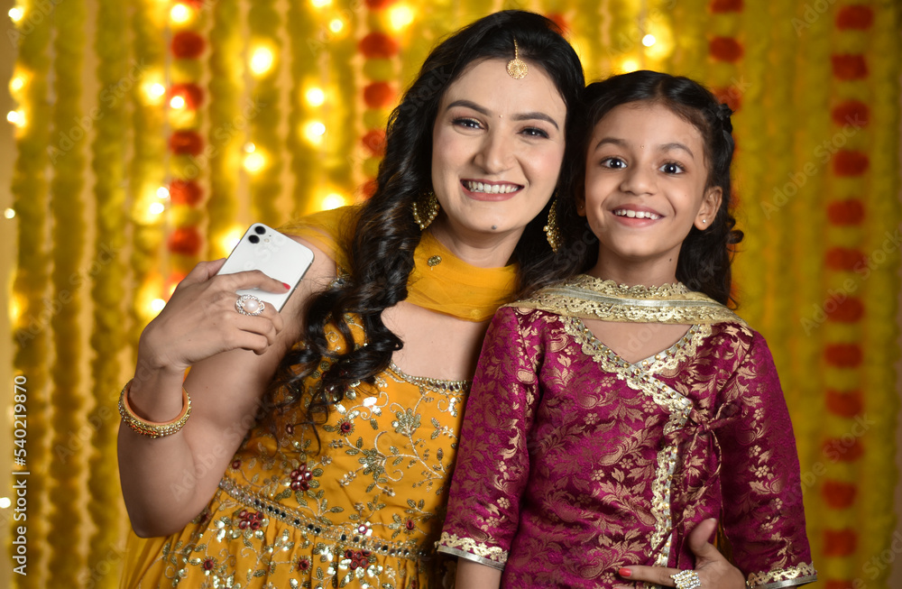 Happy Young woman and daughter celebrating diwali and clicking slefies