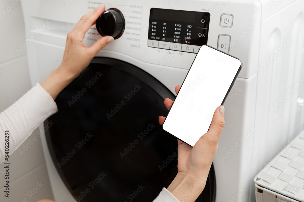 Woman pressing the button of the washing machine and holding the phone in her hands Woman pressing the button of the washing machine and holding the phone in her hands