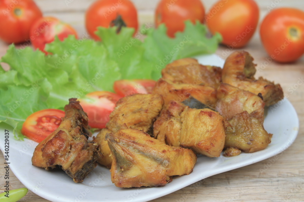 Fried chicken on a white plate with lettuce and tomato slices on a wooden table Fried chicken on a white plate with lettuce and tomato slices on a wooden table
