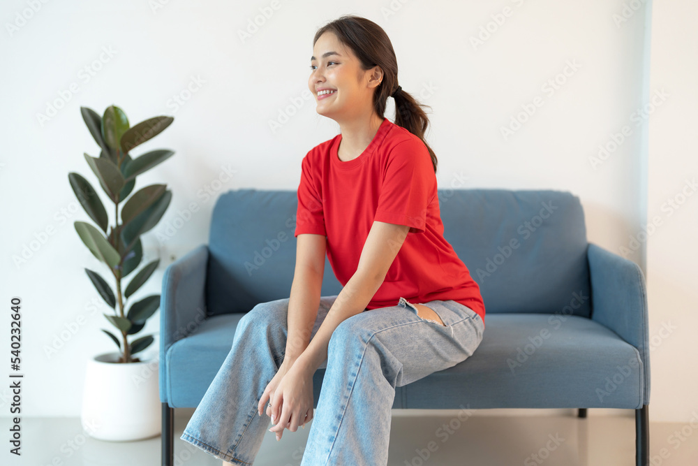 A beautiful woman in a red shirt sitting on the sofa happy smile. A beautiful woman in a red shirt sitting on the sofa happy smile.