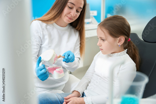 Experienced pediatric dentist teaching kid proper tooth-brushing technique