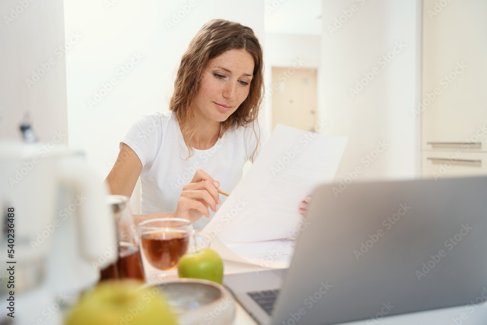 Woman reading and checking text on paper at table in kitchen Woman reading and checking text on paper at table in kitchen