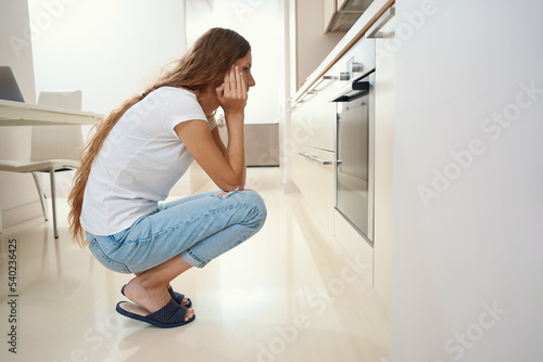 Woman sat down at oven waiting for the finished dish