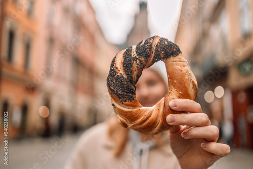 Beautiful young female tourist in stylish clothes holding pretzel obwarzanek on the market square in Krakow in Poland. High quality photo