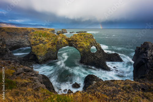 Gatklettur sea arch in Arnastapi, Snaefelsness, Iceland. Cloudy day with a rainbow. photo