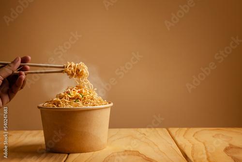 Bow of Hot Boiled Instant Noodles on the Table. Hand Using Chopsticks to Eating Noodles with Stream. Cheap Fast food Concepts. Side View with more Copy Space