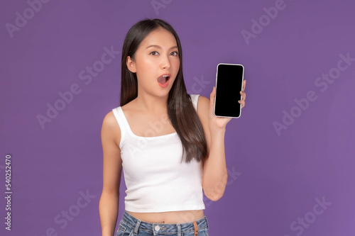 portrait of beautiful Asian young woman showing smart phone with blank screen , black screen empty copy space for advertising banner isolated on purple background , Mock Up Image