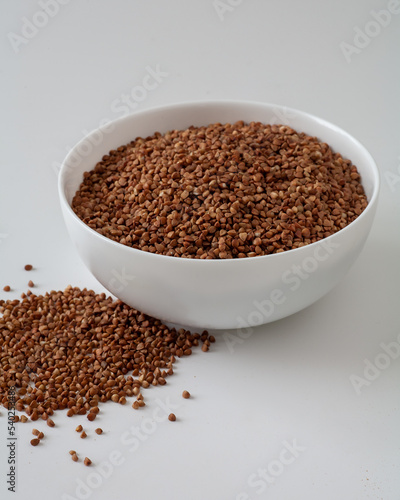There are buckwheat grains on the table in a plate. On a white background.