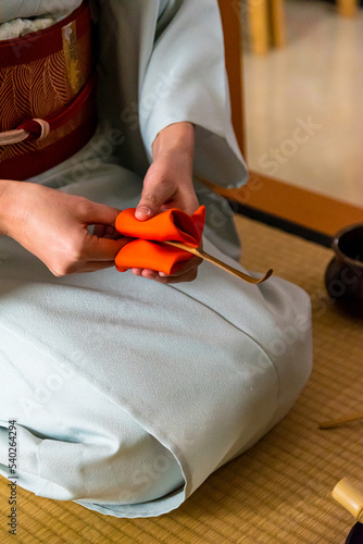 Japanese woman, tea master, Sen Rikyu, hands using an orange purifying cloth to clean a chashaku bamboo matcha tea spoon in Japanese traditional tea ceremony
