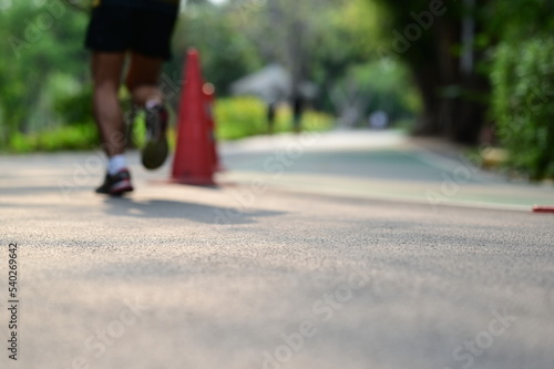 A deliberately blurred image of a man wearing black pants. Sneakers and white socks are jogging  through the orange traffic cone that divides the area for running and cycling in park early on weekend
 photo