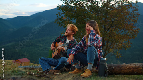 Cheerful couple enjoy nature by bonfire closeup. Young travelers play guitar.