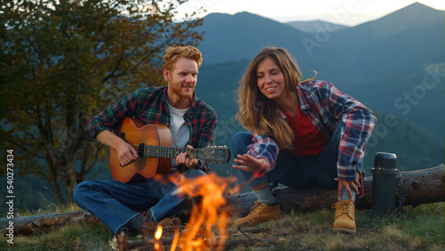 Closeup playful couple spend holiday sit bonfire. Lovers play music in mountains