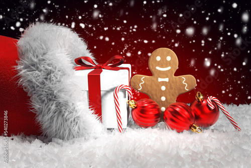Weihnachtsmütze mit Geschenk, Lebkuchen, Weihnachtskugeln und Zuckerstangen, roter Hintergrund mit Schneefall