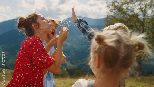Family playing blowing soap bubbles in summer mountains. Parents amusing kids.