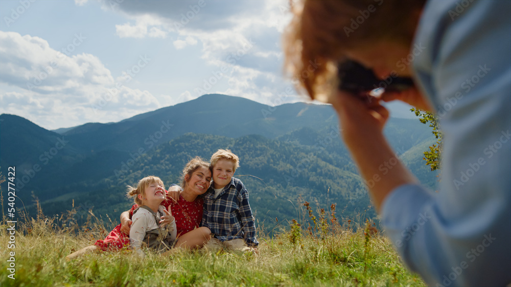Father taking photos family sitting grass mountain meadow. People enjoy summer.