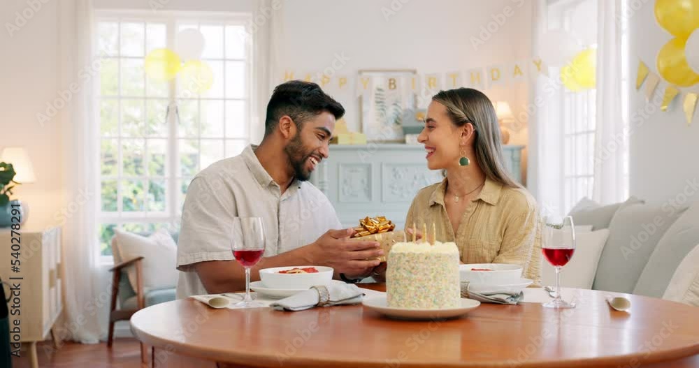 Interracial, couple and celebrate for birthday with gift, being happy and relax together at party. Romance, man and woman with present, bonding and smile in home in living room for hug or celebration Interracial, couple and celebrate for birthday with gift, being happy and relax together at party. Romance, man and woman with present, bonding and smile in home in living room for hug or celebration