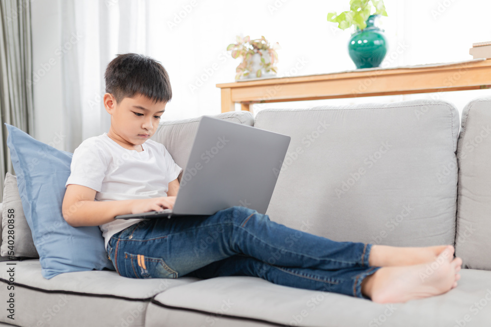 Asian boy learning to use laptop, he feel fun and happy about online education, he search information and study in home, network and technology Asian boy learning to use laptop, he feel fun and happy about online education, he search information and study in home, network and technology