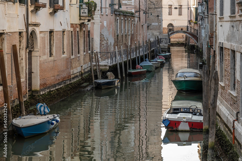 Small, Venetian canal, located off the main areas of Venice. Small boats can be seen moored against the doors opening up to the water