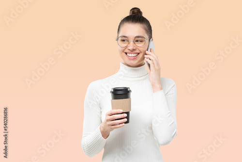 Smiling woman talking on phone, laughing at jokes, holding coffee to go cup on brown background