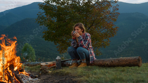 Lonely traveler rest forest in mountains. Relaxed woman drink tea by campfire. © stockbusters