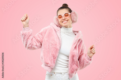 Smiling dancing woman in pink trendy fluffy bomber, ear warmers or winter headphones and glasses photo