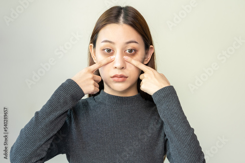 Fotografie, Obraz Bored, insomnia asian young woman, girl looking at camera, hand touching under eyes with problem of black circles or panda puffy, swollen and wrinkle on face