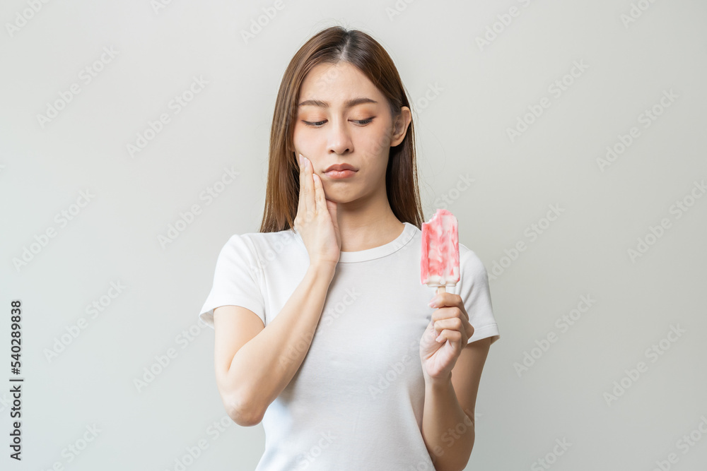 Face expression suffering from sensitive teeth and cold, asian young woman, girl hand touching her cheek, feeling hurt, pain eating ice cream, lolly. Toothache molar tooth at home, dental problem. Face expression suffering from sensitive teeth and cold, asian young woman, girl hand touching her cheek, feeling hurt, pain eating ice cream, lolly. Toothache molar tooth at home, dental problem.