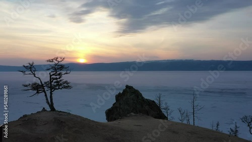 Drone view of sunset on the Baikal lake. Beautiful landscape on Olkhon island. Shamanka rock or cape Burkhan. Spring in Siberia. Lonely tree and mountains in the evening time photo