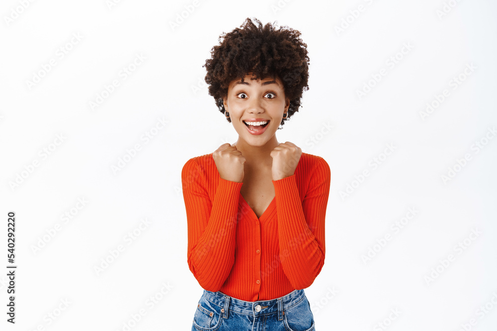 Enthusiastic african american woman jumps from excitement, looks surprised and thrilled, stands over white background