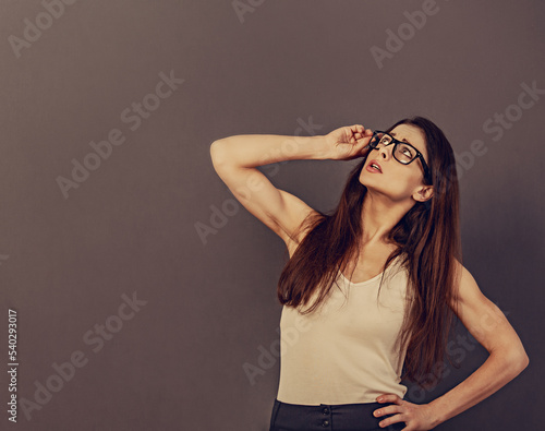Beautiful positive business thinking woman in eyewear in white t- shirt looking up on empty copy space grey background. Closeup
