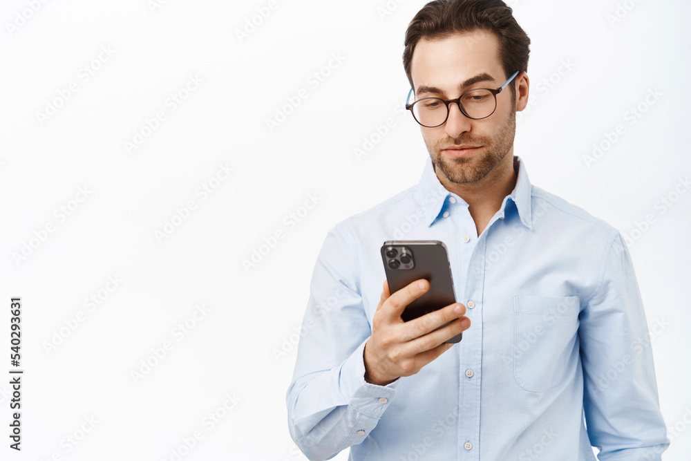 Handsome male entrepreneur using mobile phone, standing in glasses and blue shirt over white background Handsome male entrepreneur using mobile phone, standing in glasses and blue shirt over white background