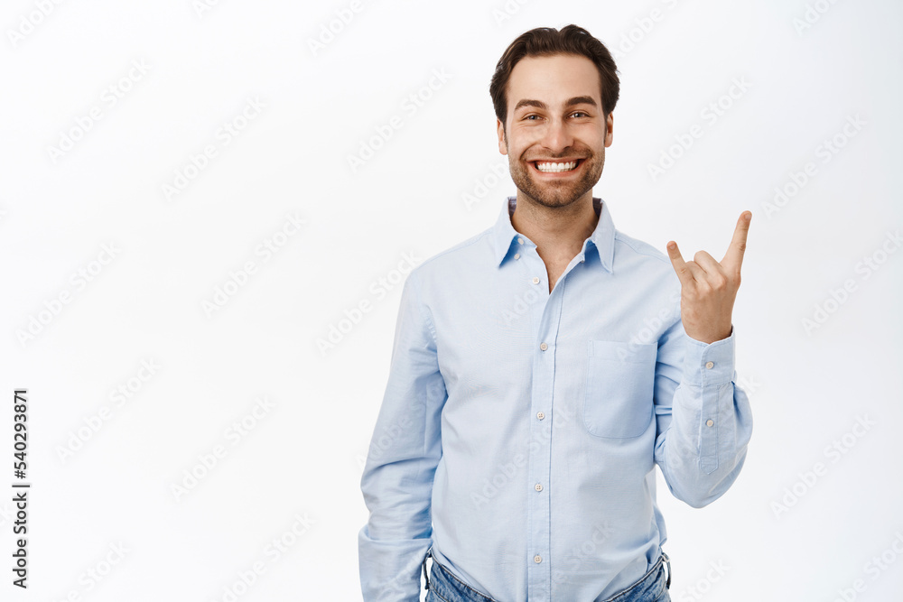 Happy office guy shows rock on, heavy metal horns sign and smiles pleased, has fun, stands over white background Happy office guy shows rock on, heavy metal horns sign and smiles pleased, has fun, stands over white background